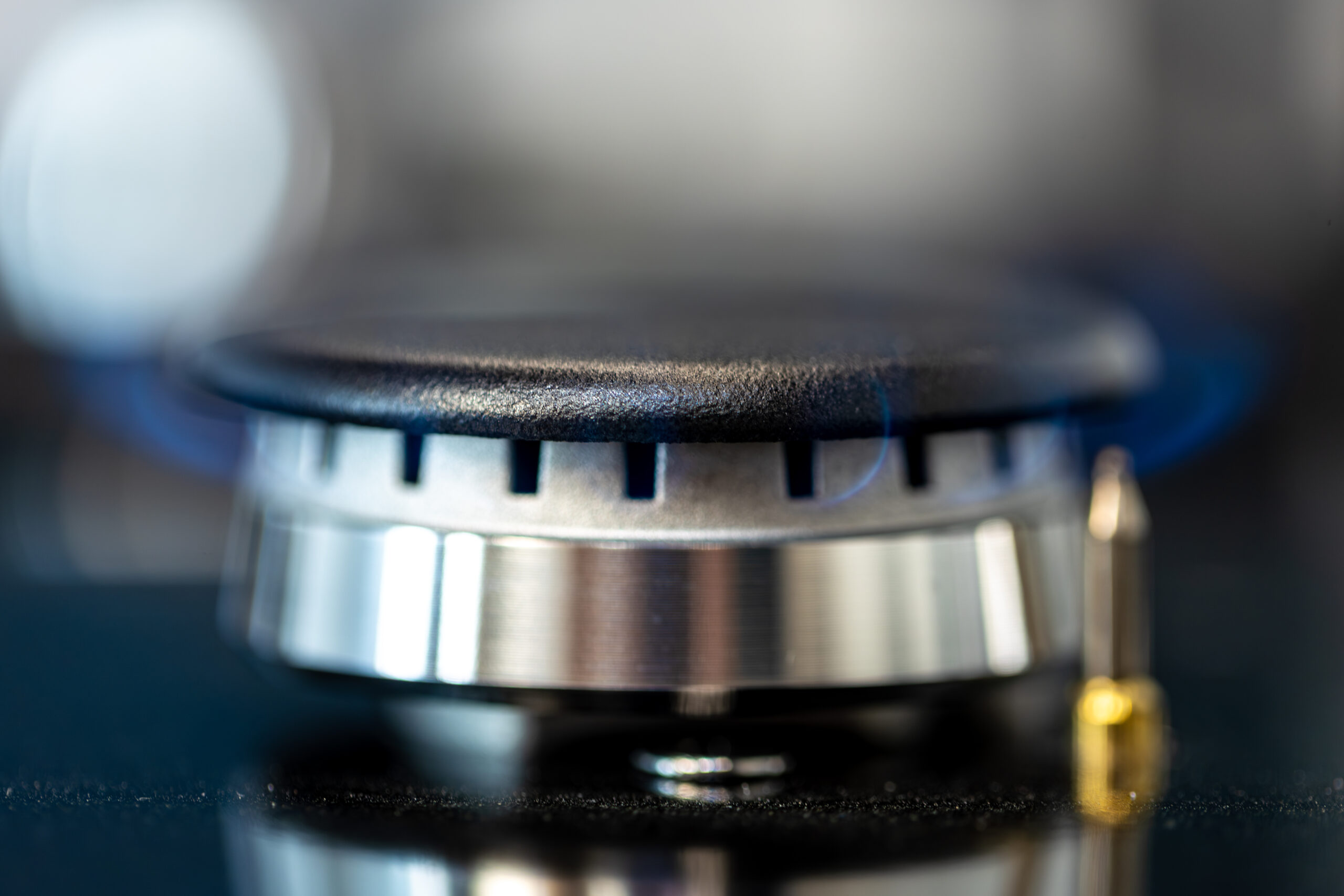 Stainless steel gas burner with visible flame captured in sharp macro detail. A blend of power, precision and modern kitchen technology.